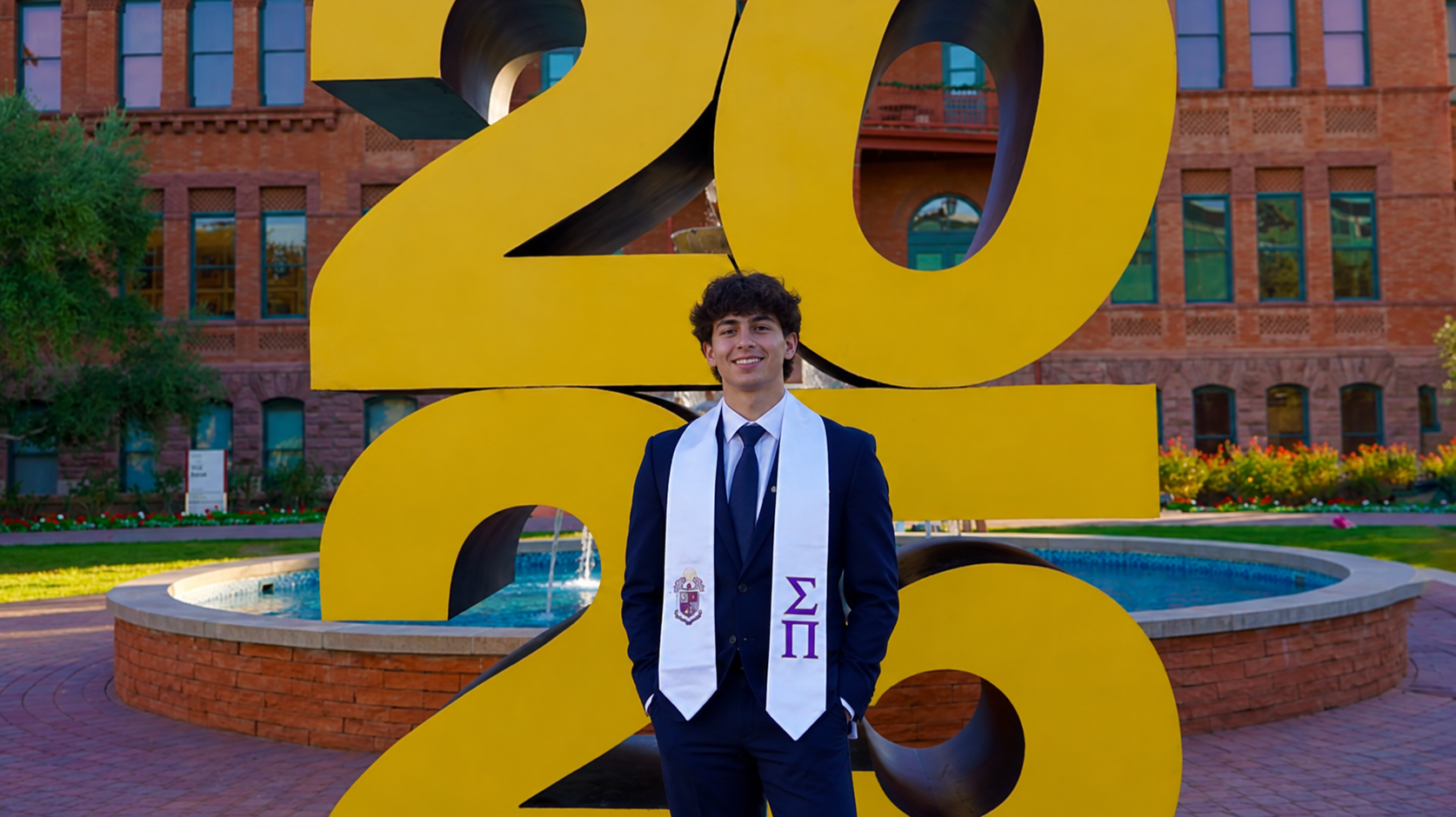 Graduate in cap and gown regalia at the ASU 2025 sign